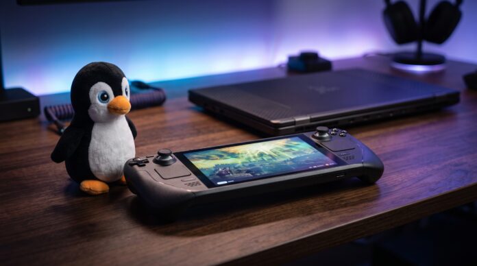 Consola portátil de PC para juegos junto a un pingüino de peluche y una laptop